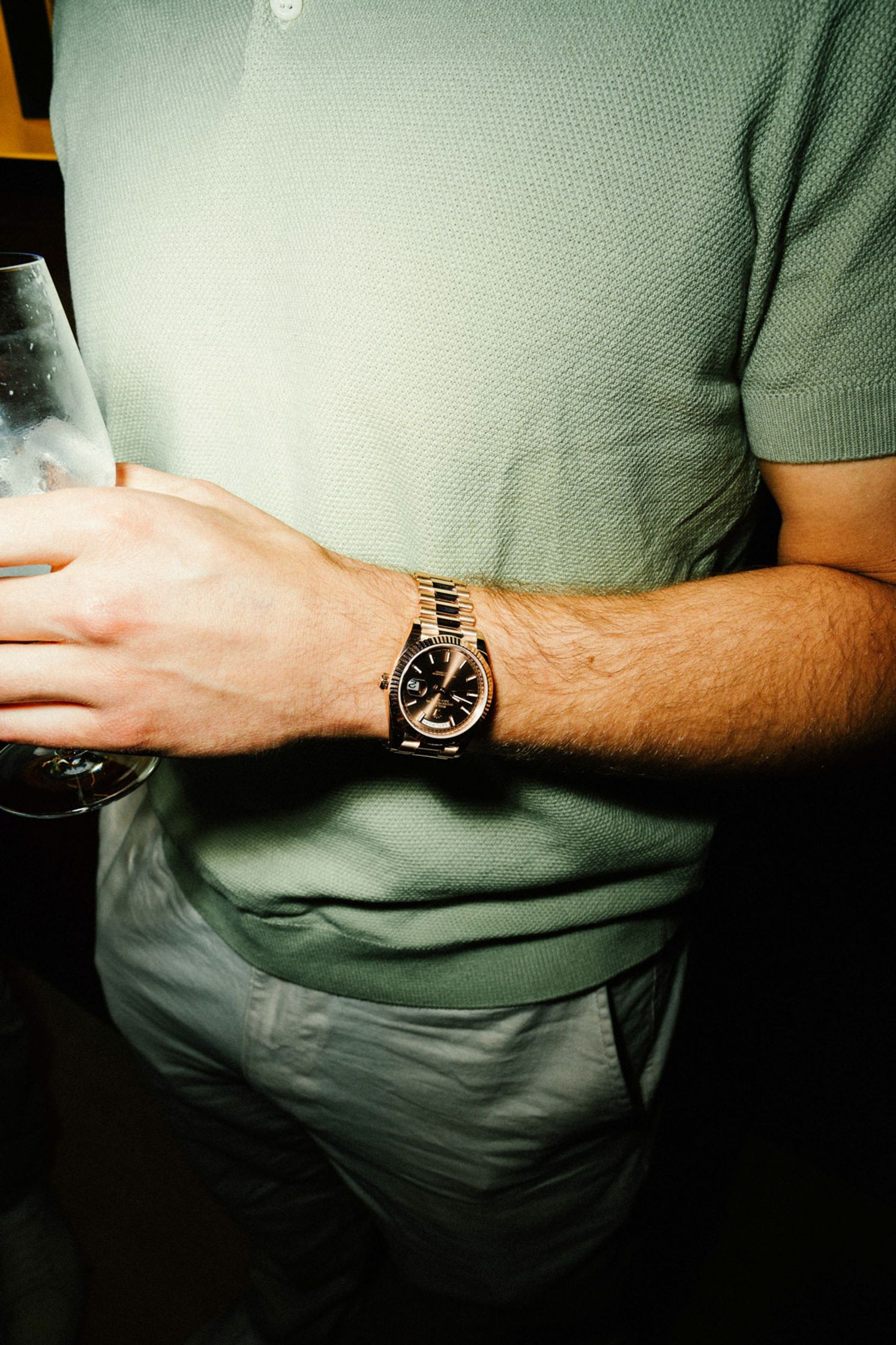 Nahaufnahme eines Mannes im salbeigrünen Polo mit goldener Rolex Datejust am Handgelenk und Weinglas – Rolex Boutique Event Berlin