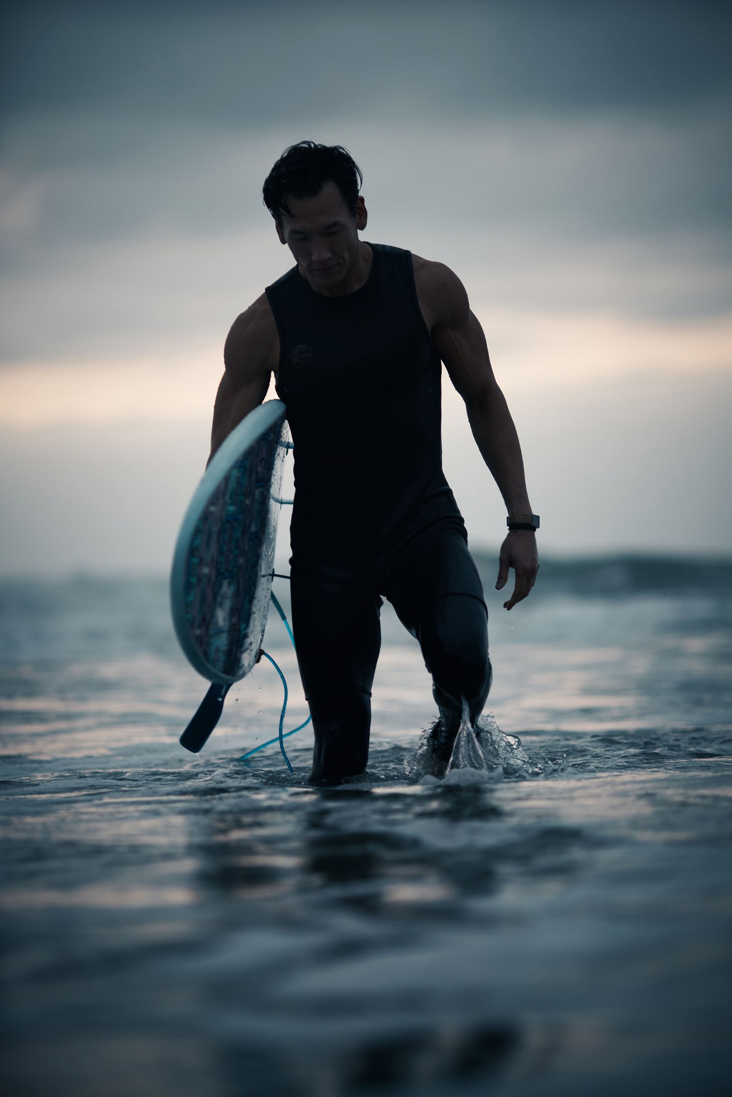 a man walking into the ocean with a surfboard