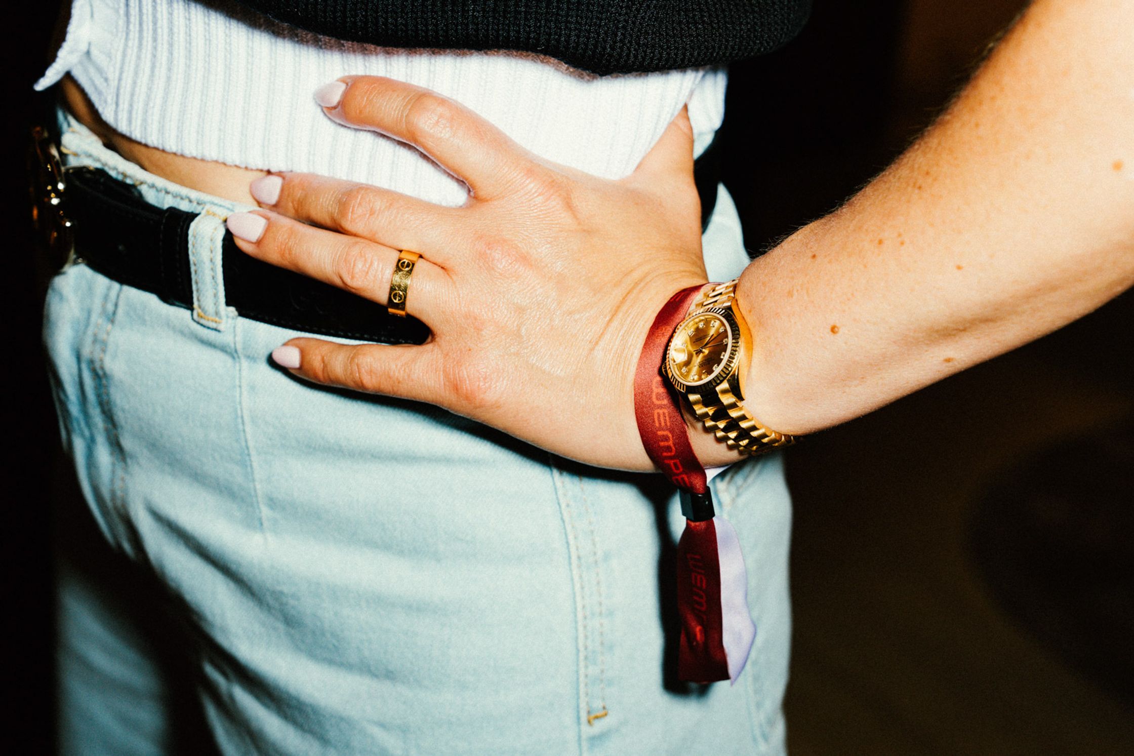 Detailaufnahme Handgelenk: Goldene Rolex Datejust Uhr und Cartier Love Ring an weiblicher Hand, rotes Event-Bändchen am Handgelenk, Jeans mit Gürtel beim Rolex Boutique Event Berlin