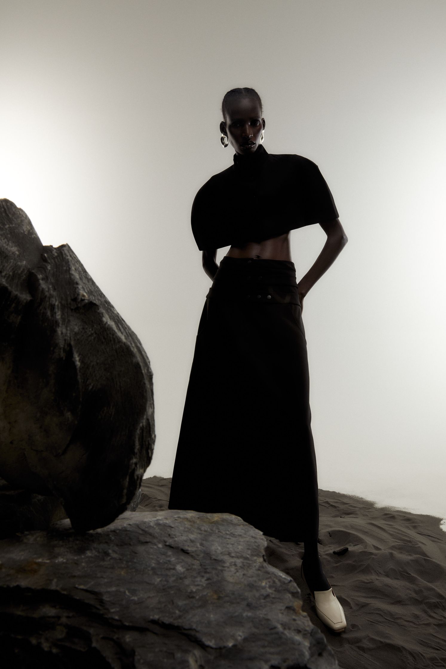 a woman in a black skirt standing on a rock