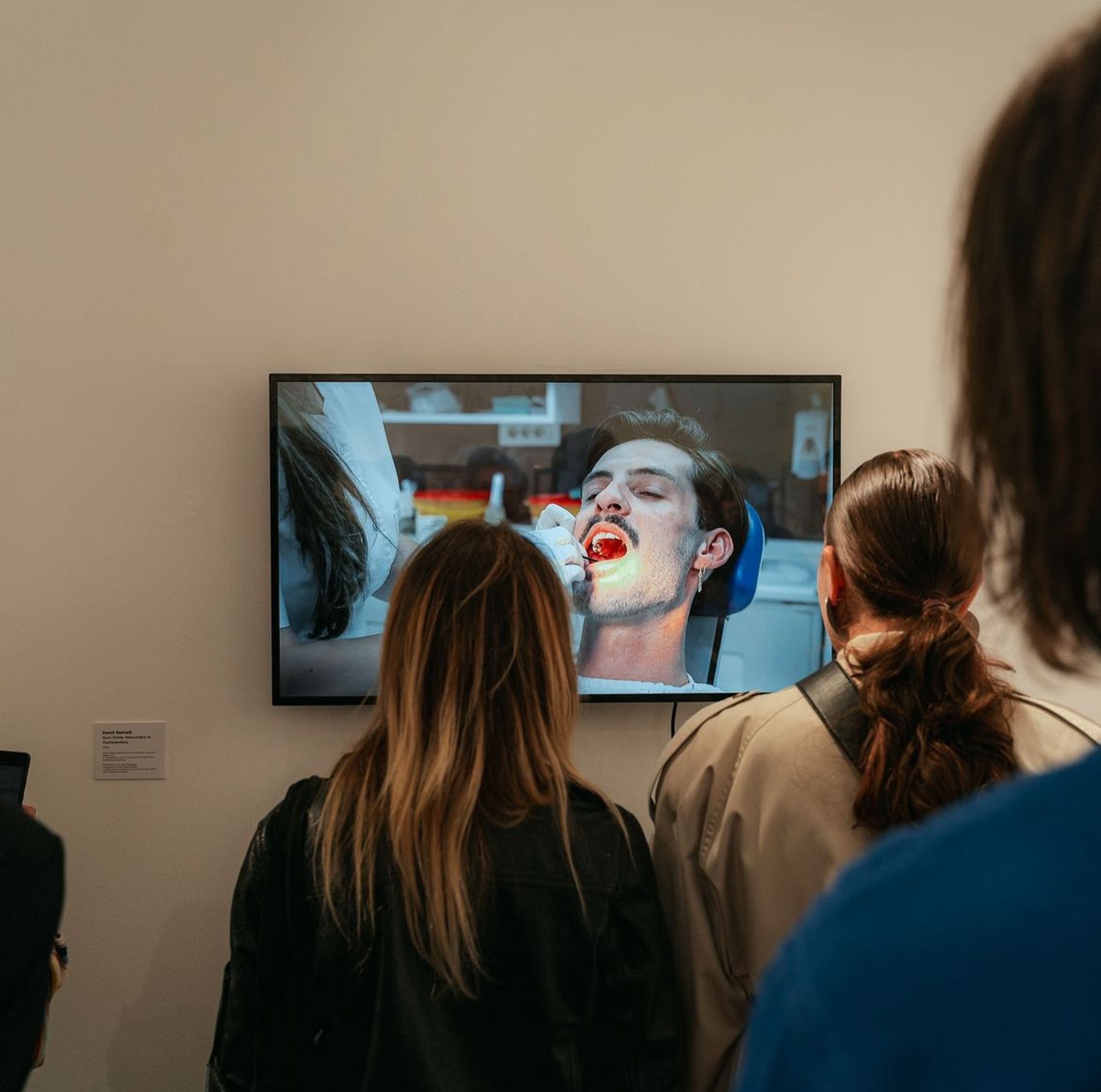 Audience members viewing a video installation of a man undergoing a dental procedure.