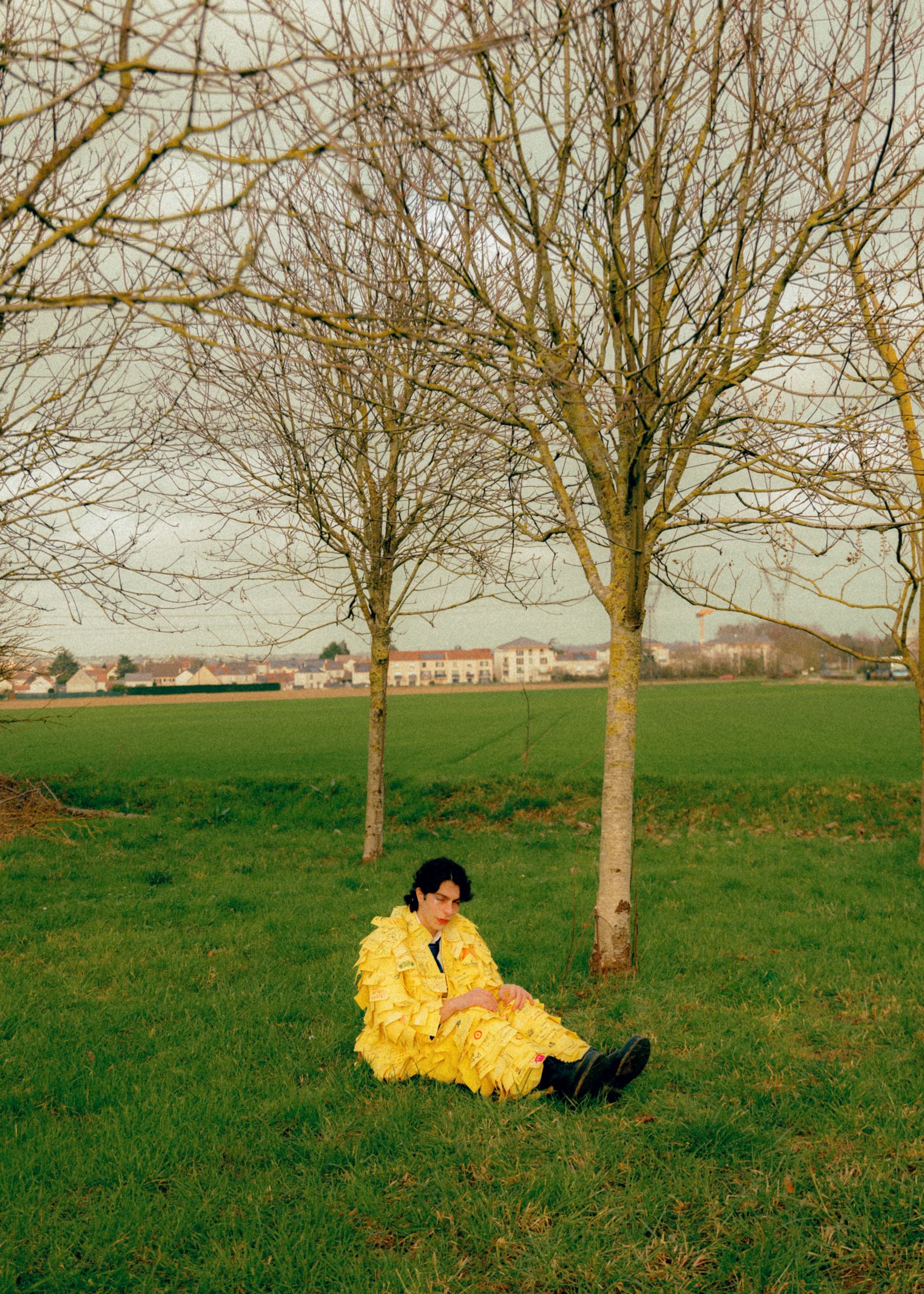 a fashion editorial of a man in a yellow suit sitting in a field