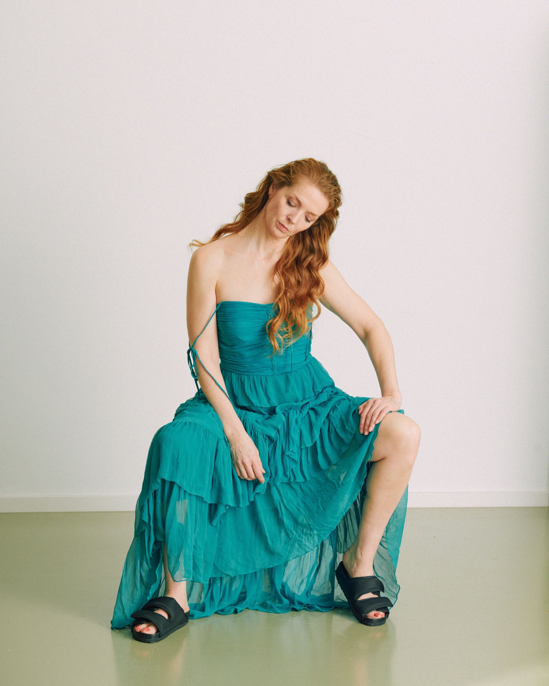 Pheline Roggan woman in a teal dress sitting on the floor