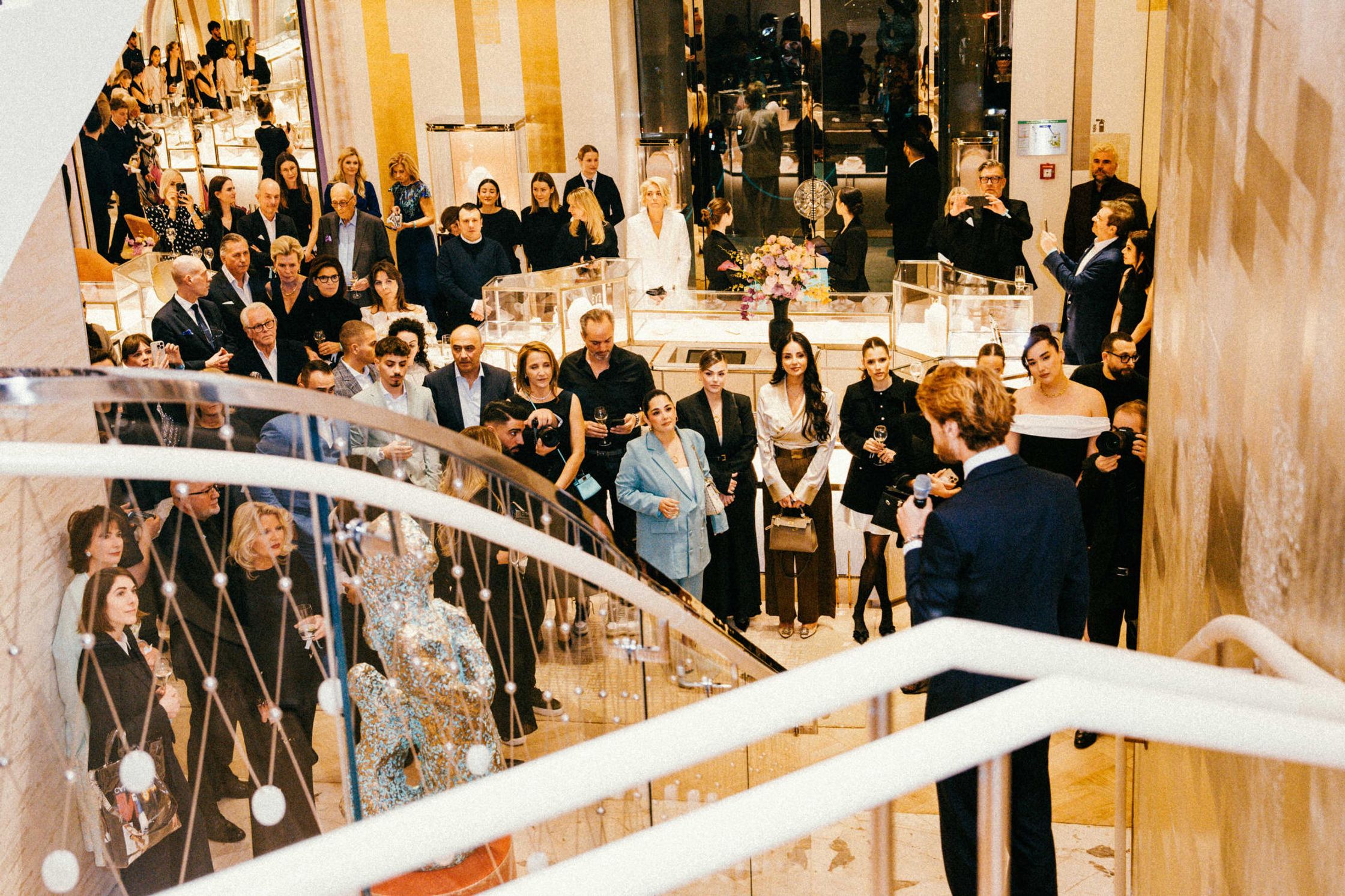 Blick von der Treppe auf zahlreiche Gäste beim Tiffany & Co. Event Berlin – Mann mit Mikrofon hält Rede, Schmuckvitrinen und Torso-Skulptur im Hintergrund