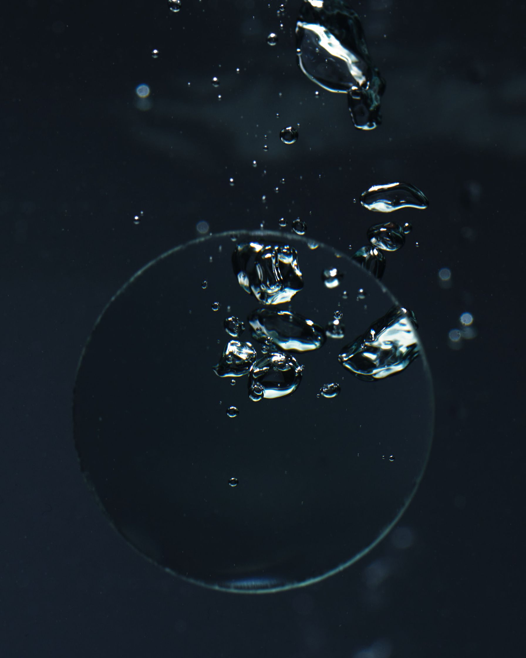 Convex glass disc creating bubbles underwater, emphasizing light distortion and fluidity.