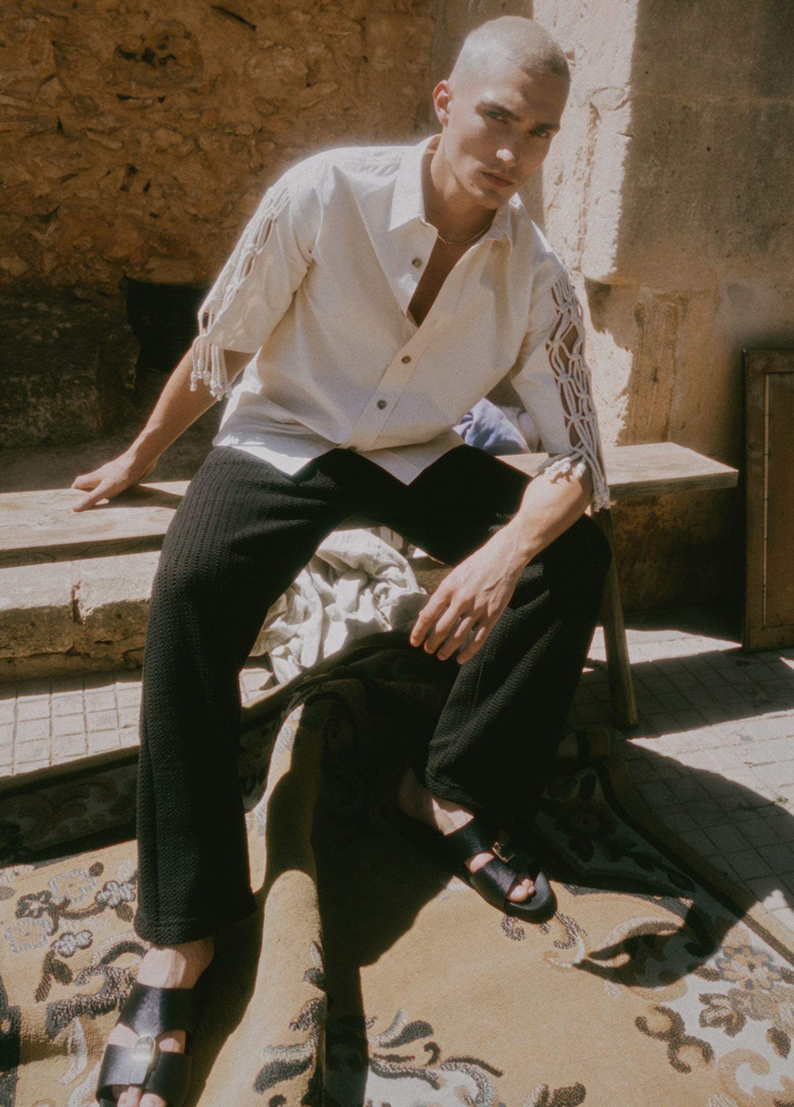 a man wearing a white shirt and sandals sitting on a rug