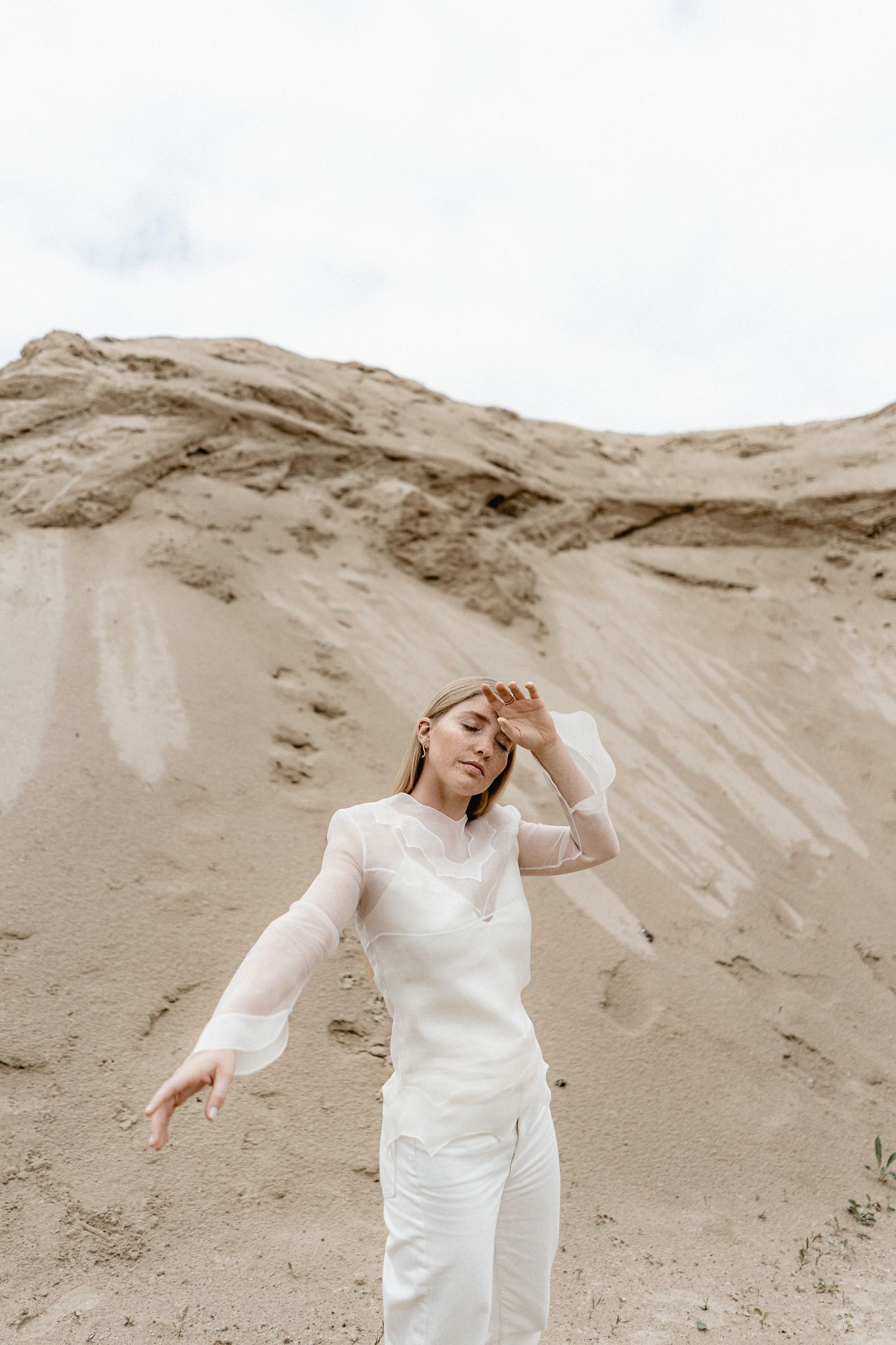 a model posing in white in front of a sand dune with maren jewellery earings