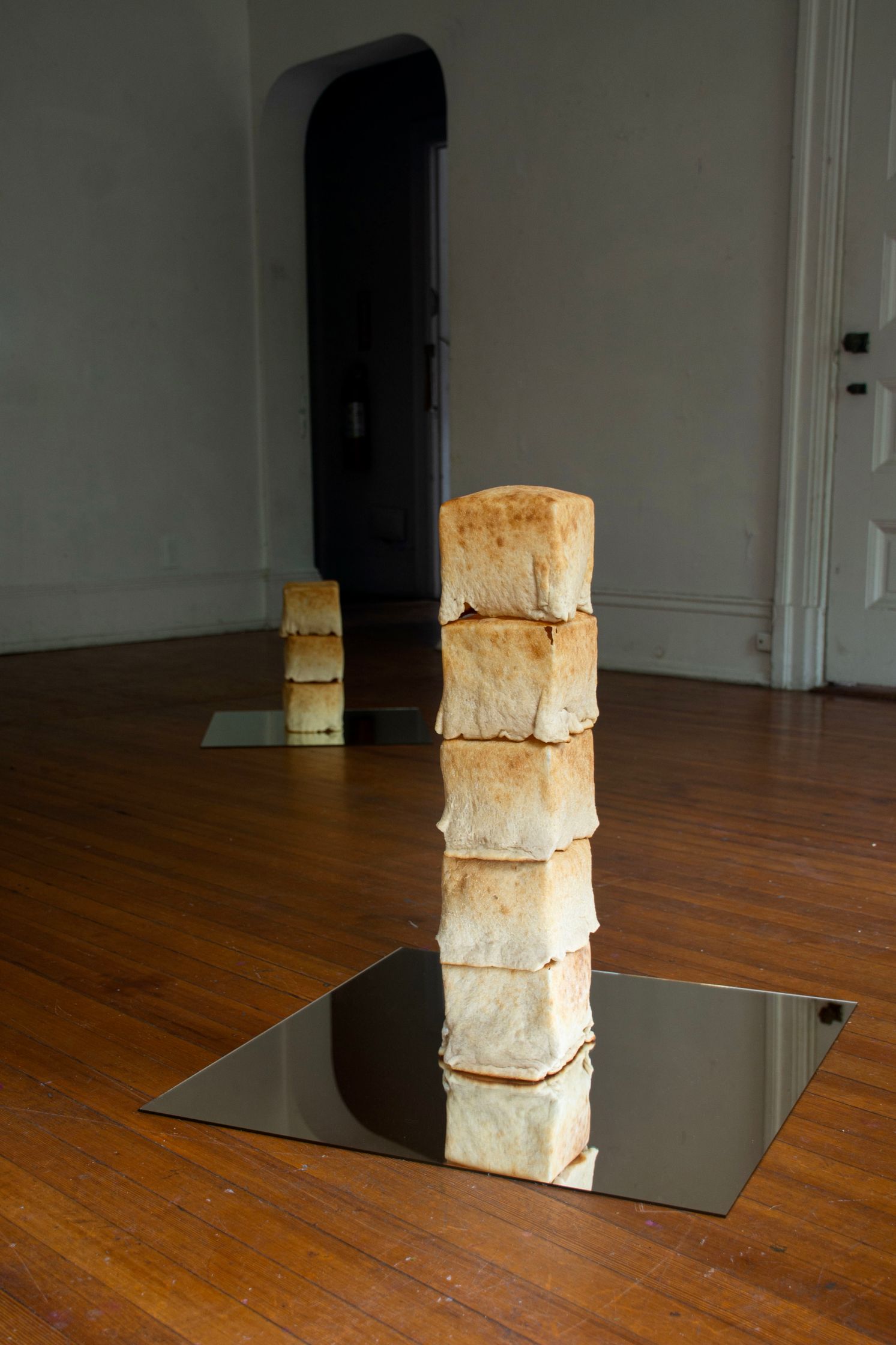 Two stacks of cubed bread loaves on reflective surfaces on a wooden floor in a dimly lit room.