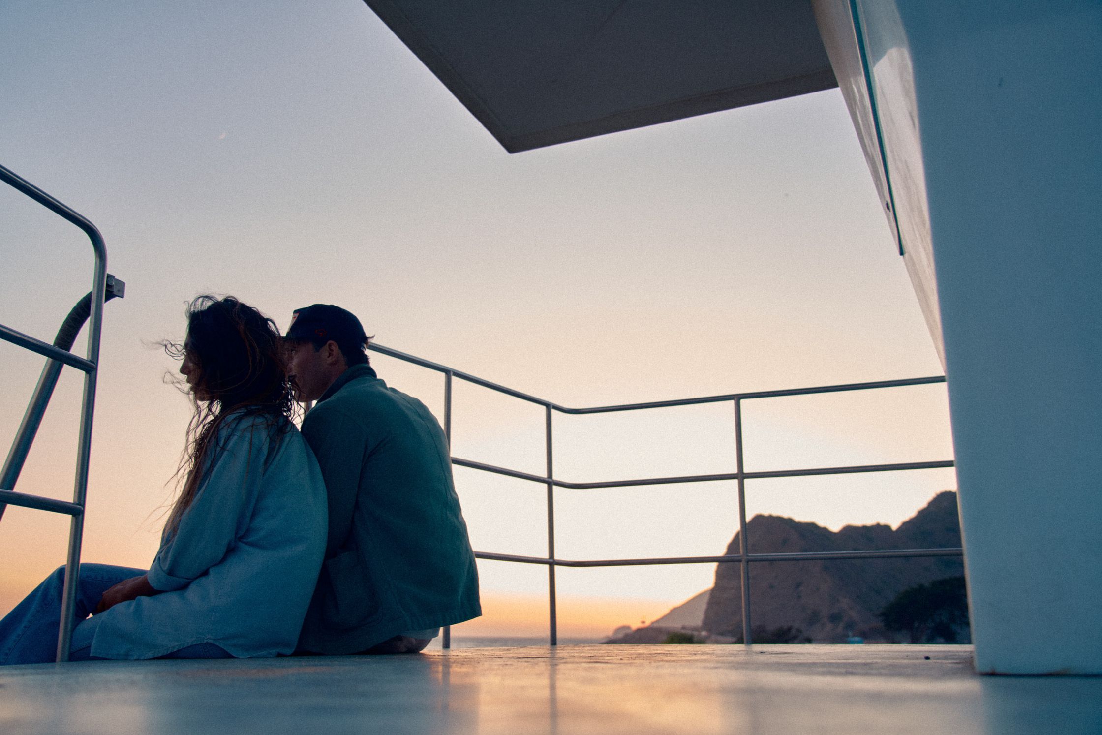 a couple sitting on the deck of a boat at sunset
