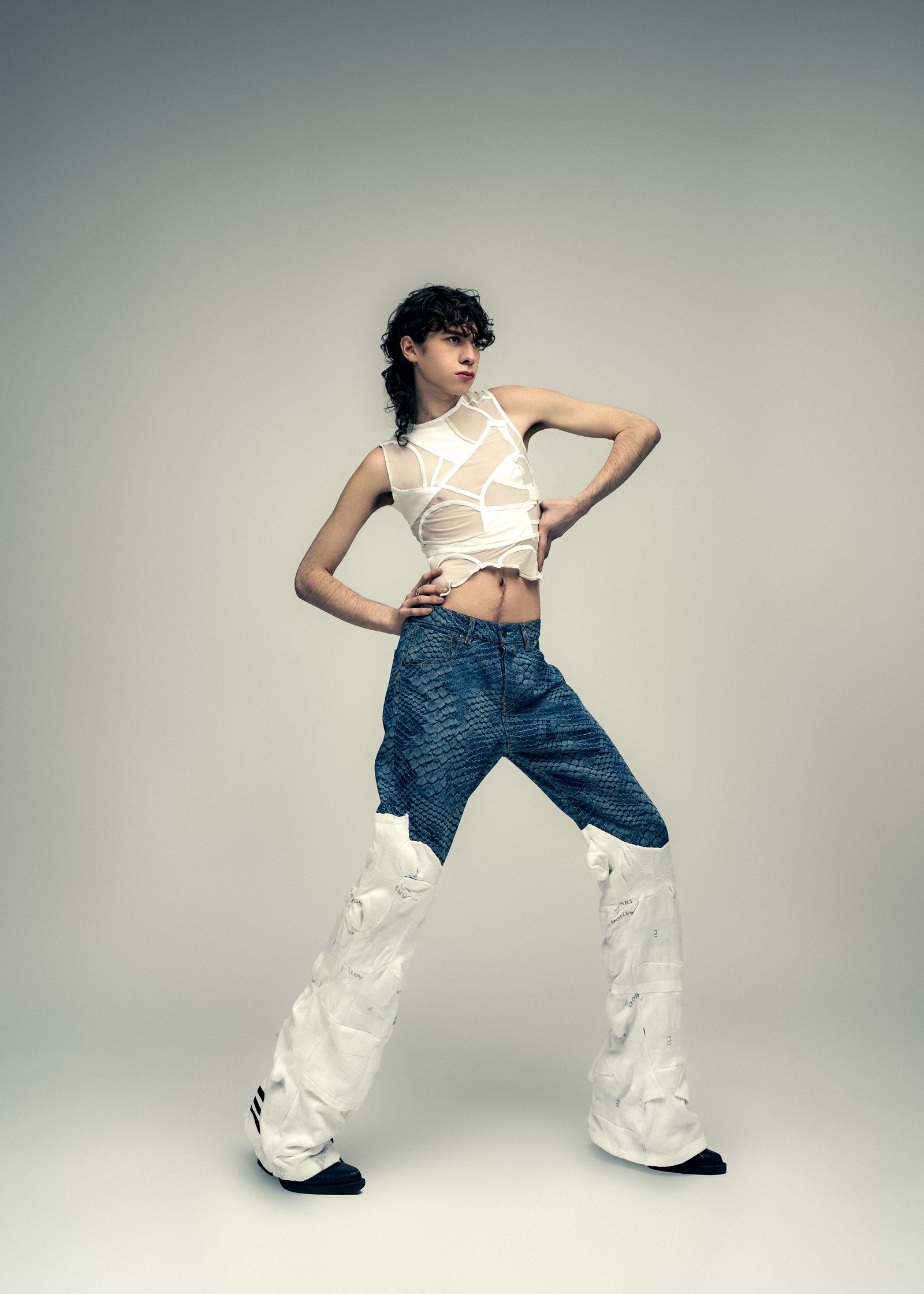 a man in a white top and jeans posing on a gray background