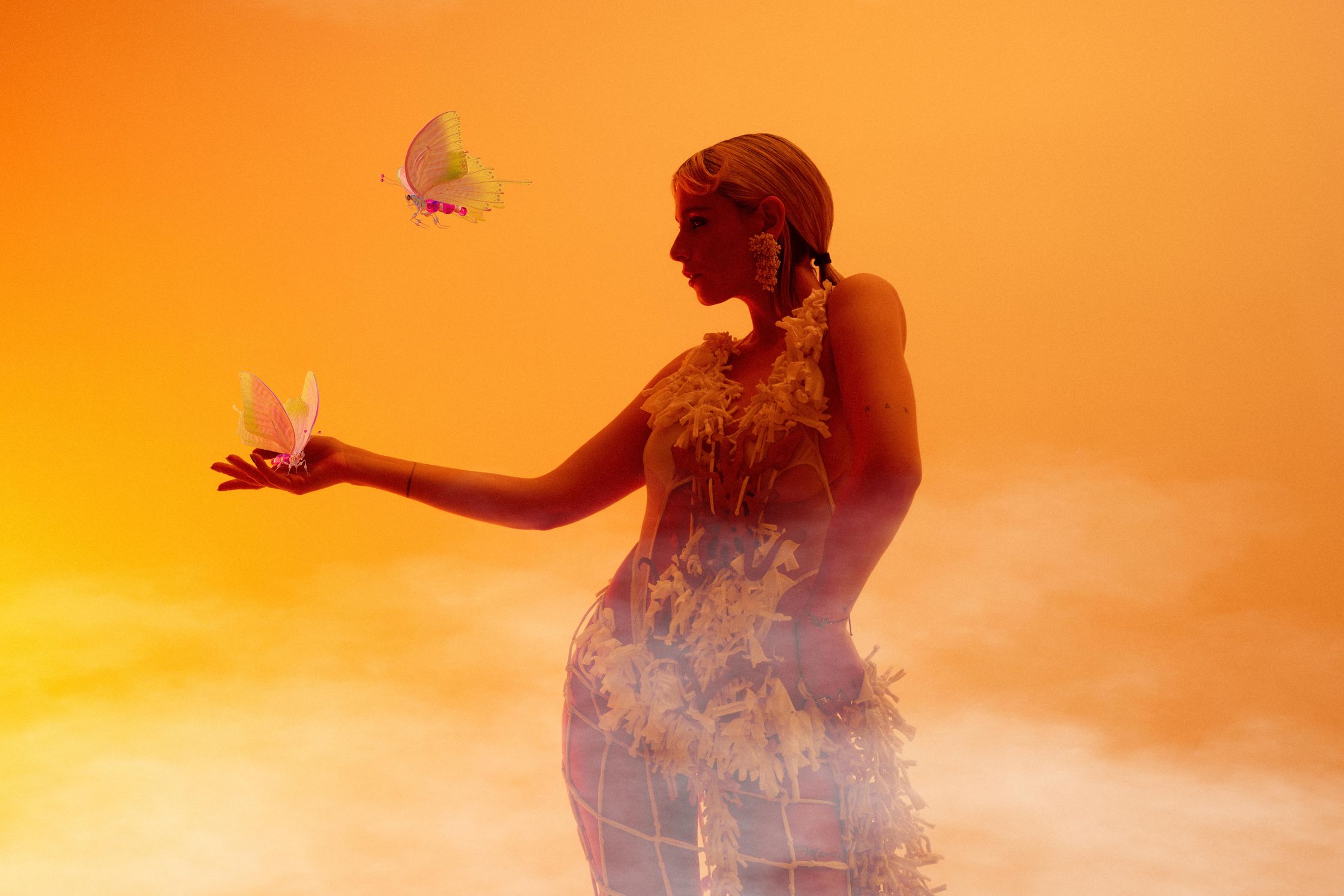 a woman is holding a butterfly in front of an orange sky