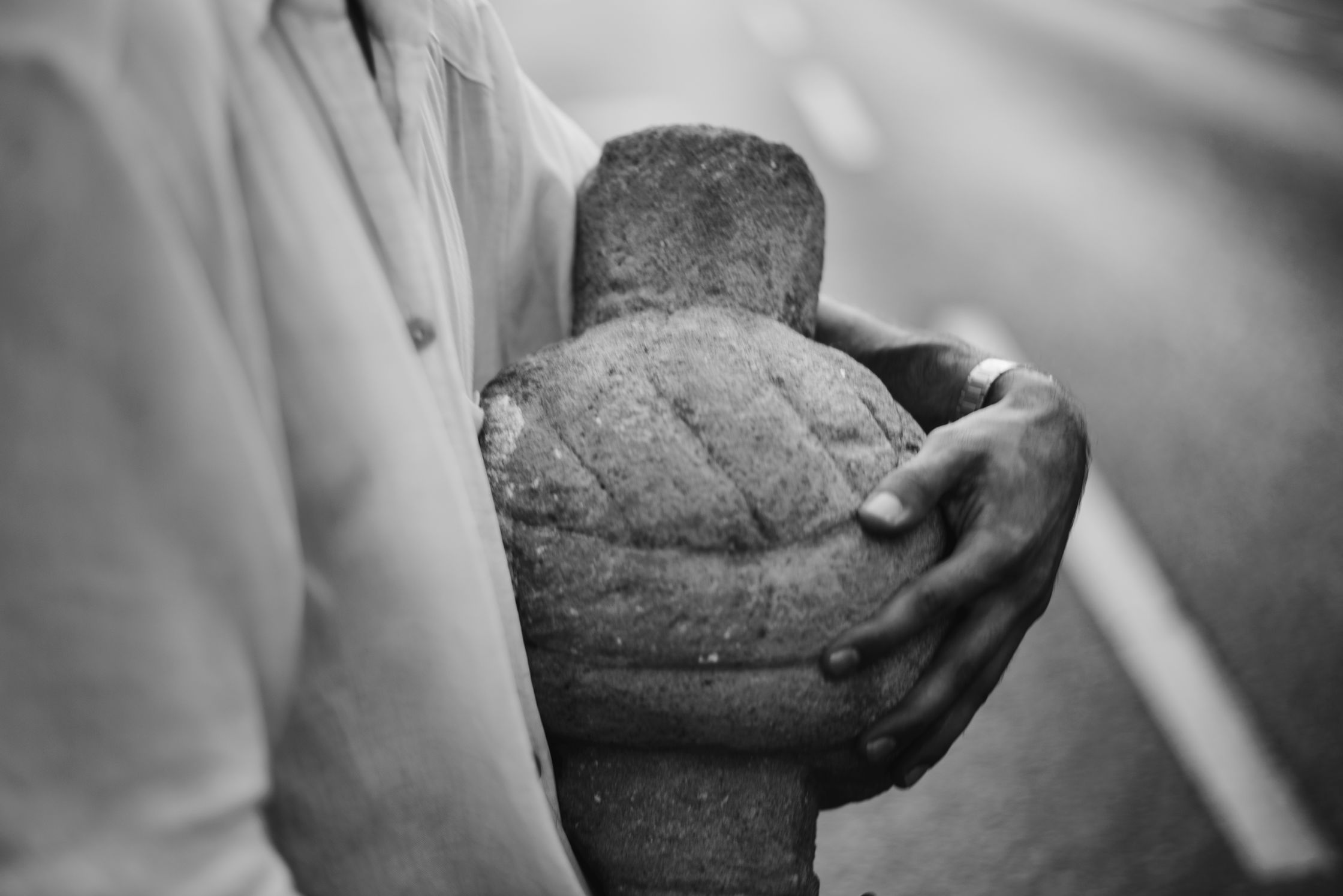 A person in a light-colored shirt holding a weathered stone sculpture of a body.