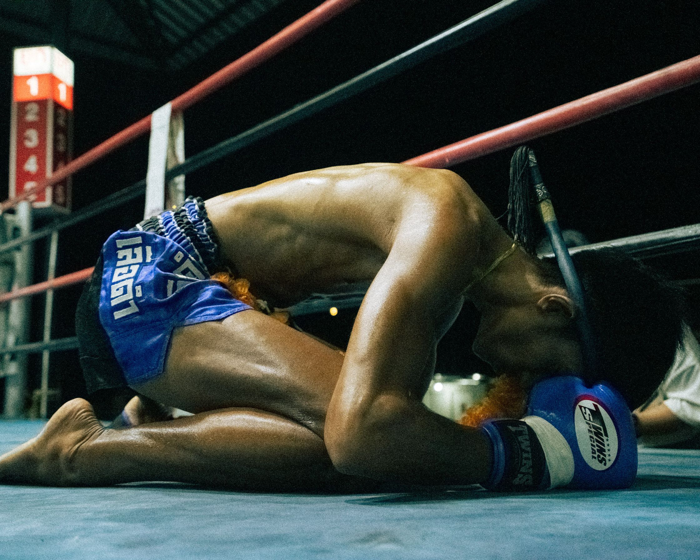 A Muay Thai fighter kneeling on the ground in prayer, deeply focused on traditional rituals and spirituality within the ring at Koh Tao.
