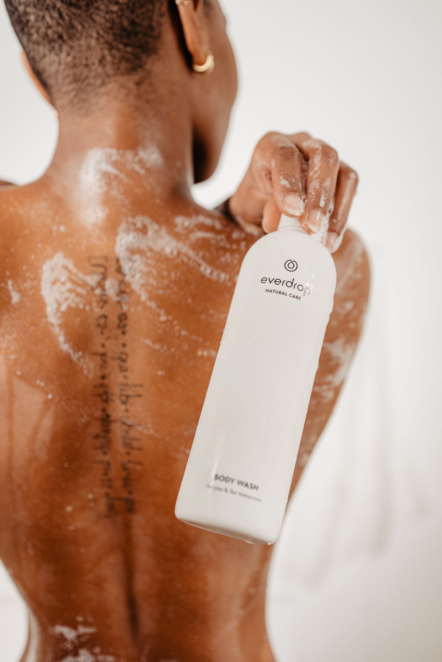 a woman holding a bottle of everdrop body wash on her back