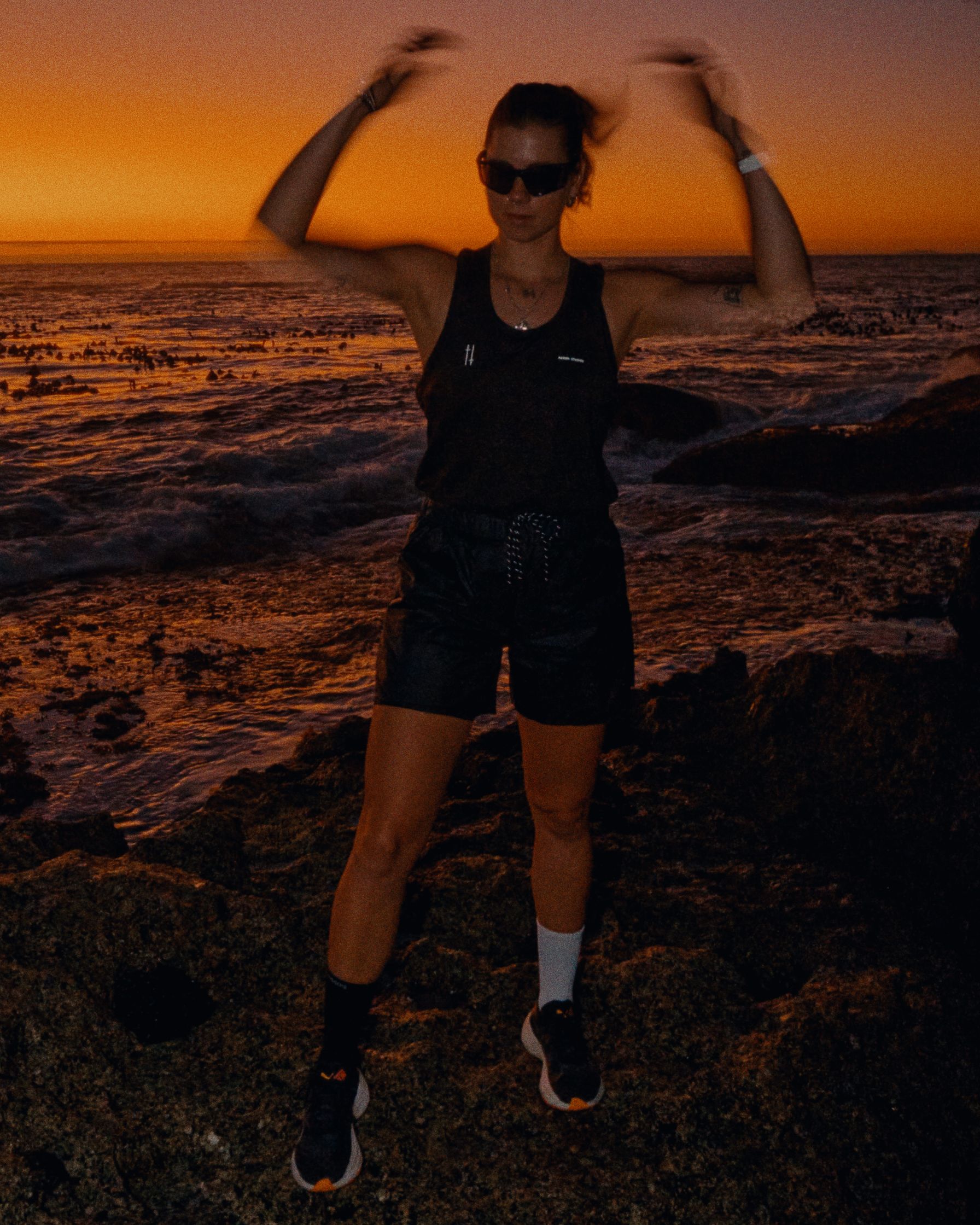 a woman wearing a black tank top and shorts at sunset