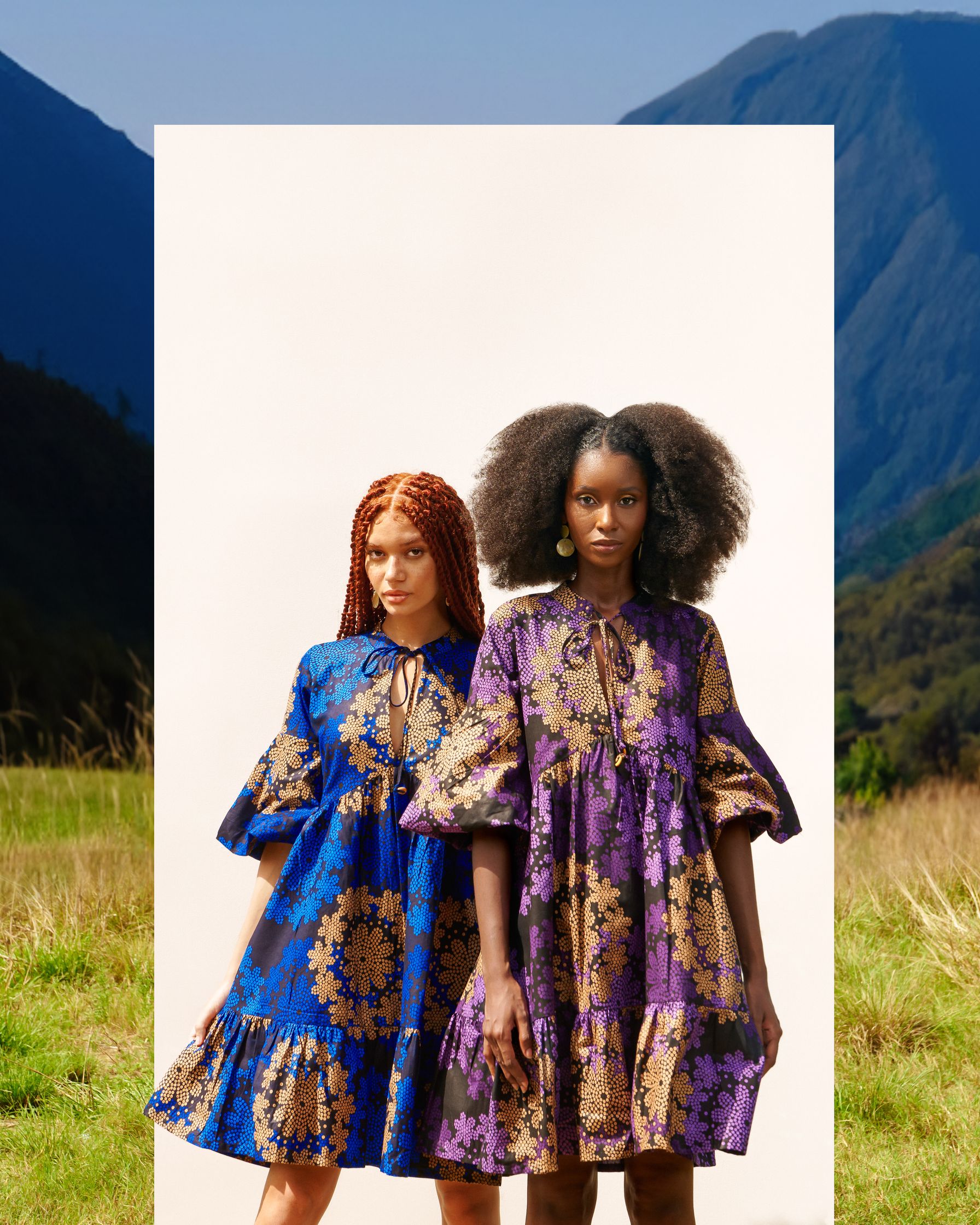 two women standing in front of a field with mountains in the background