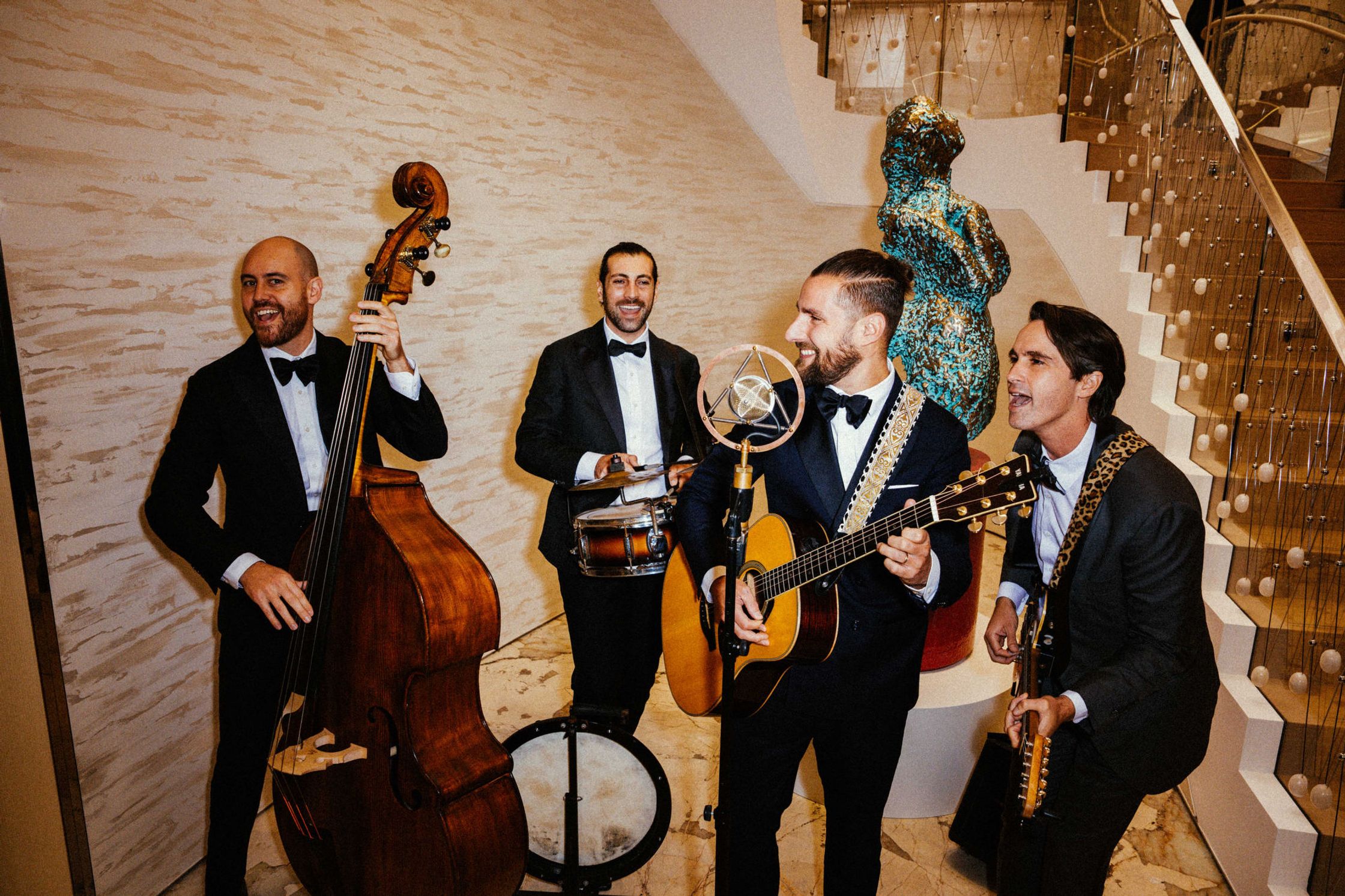 Vierköpfige Live-Band in Smokings beim Tiffany & Co. Event Berlin – Kontrabass, Snare-Drum, Akustikgitarre und Sänger an einem Vintage-Mikrofon neben einer Treppe