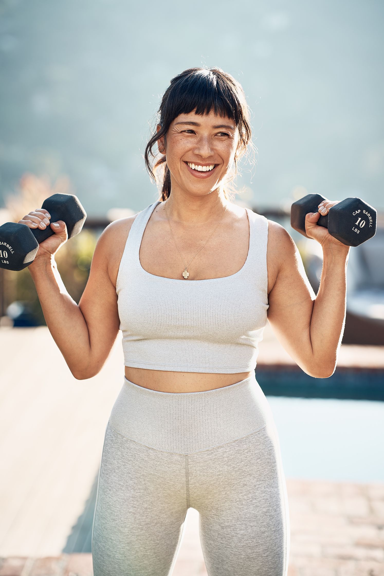 a woman holding two dumbbells in front of a pool