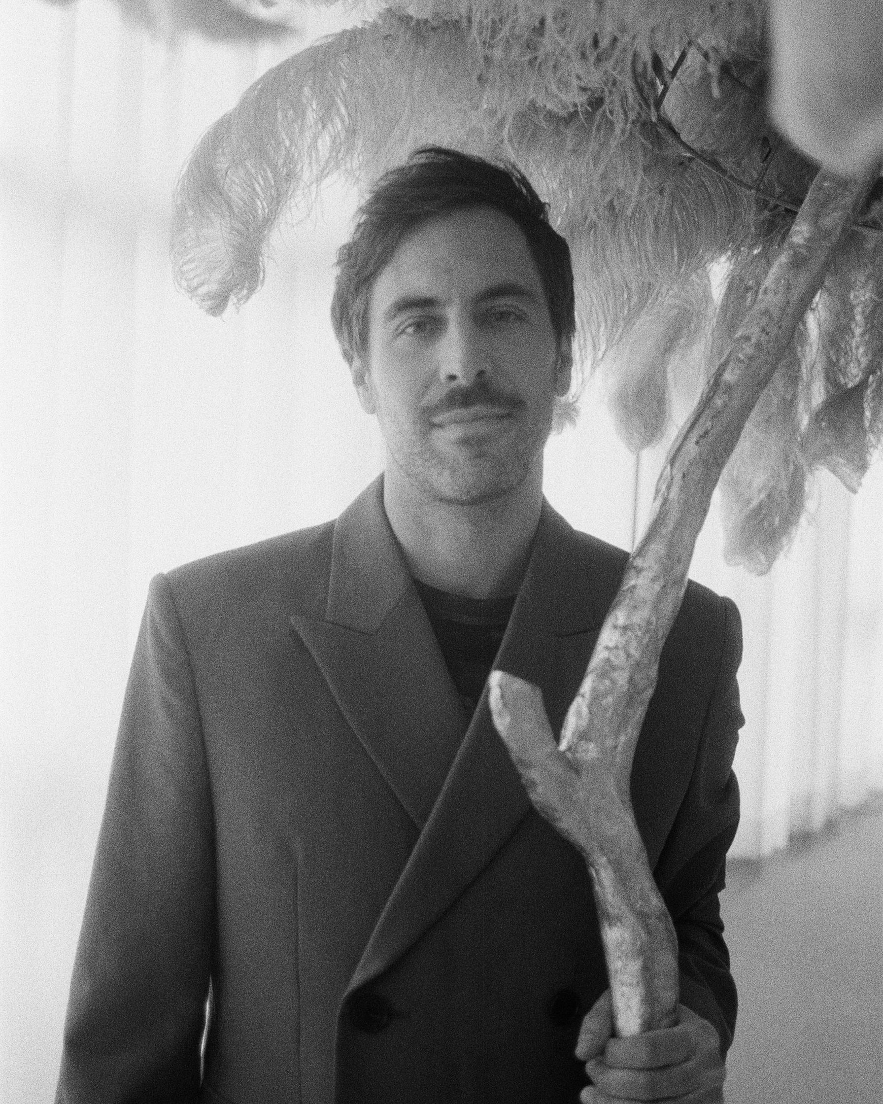 Max Giesinger in a suit standing next to a feathered tree