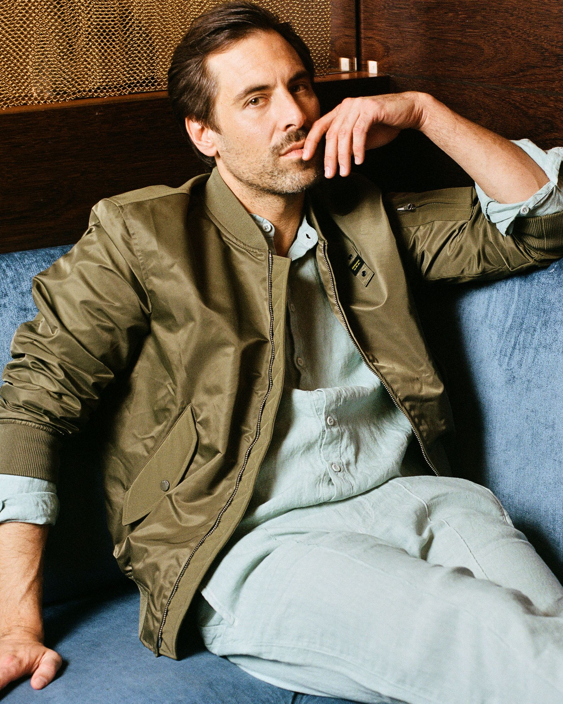 Max Giesinger in a green bomber jacket sitting on a blue couch
