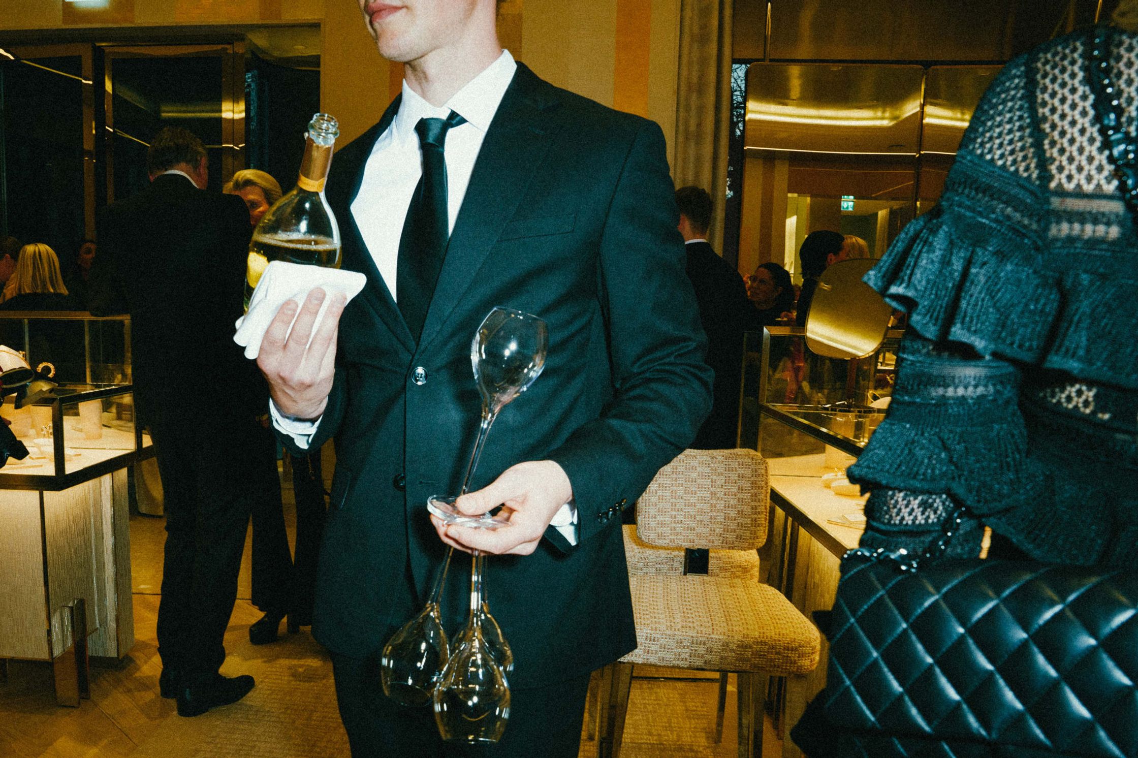 Kellner im schwarzen Anzug trägt Champagnerflasche und mehrere Gläser beim Tiffany & Co. Event Berlin – Schmuckvitrinen und Gäste im Hintergrund