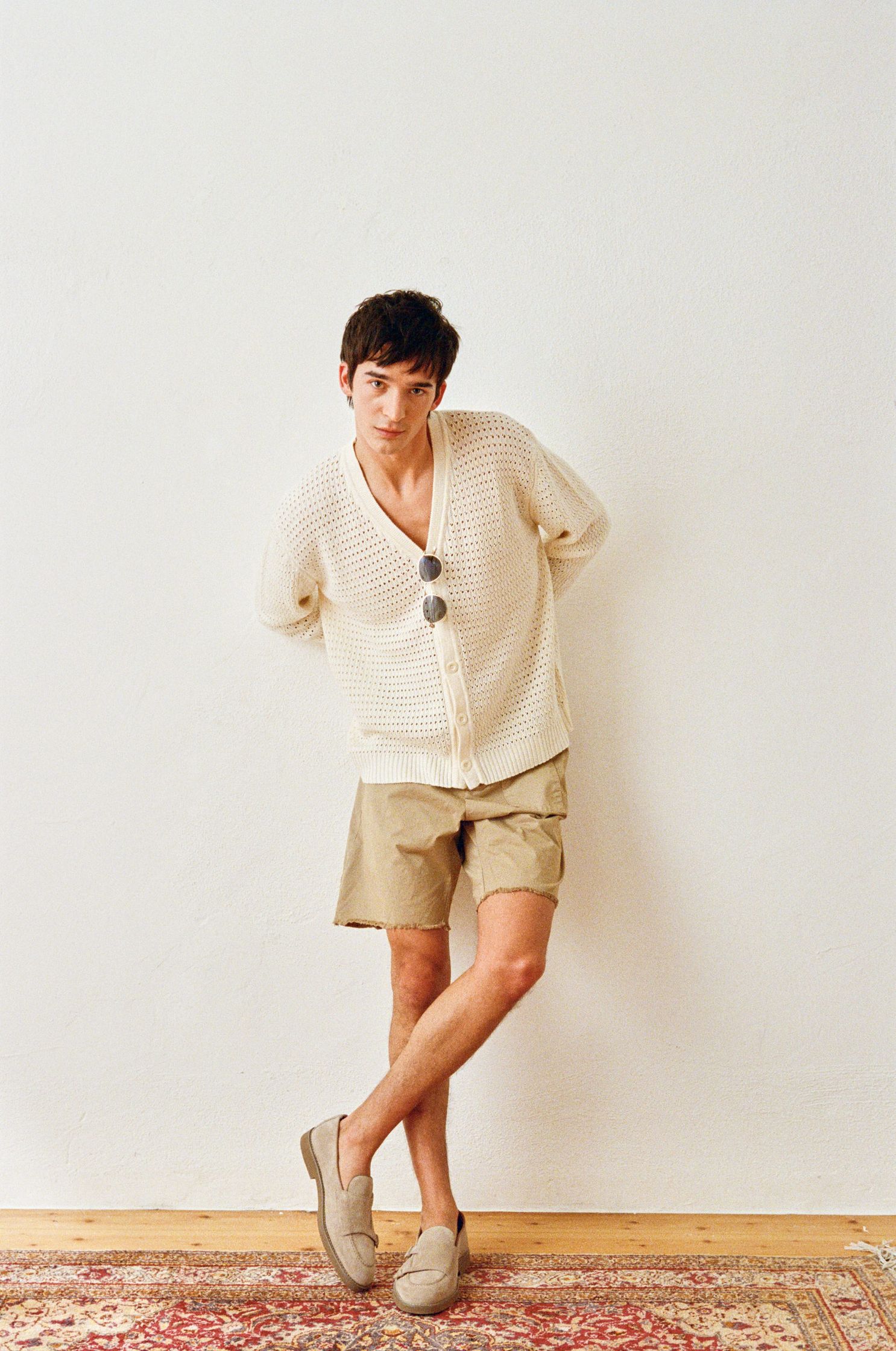 a man in a tan sweater and shorts leaning against a rug
