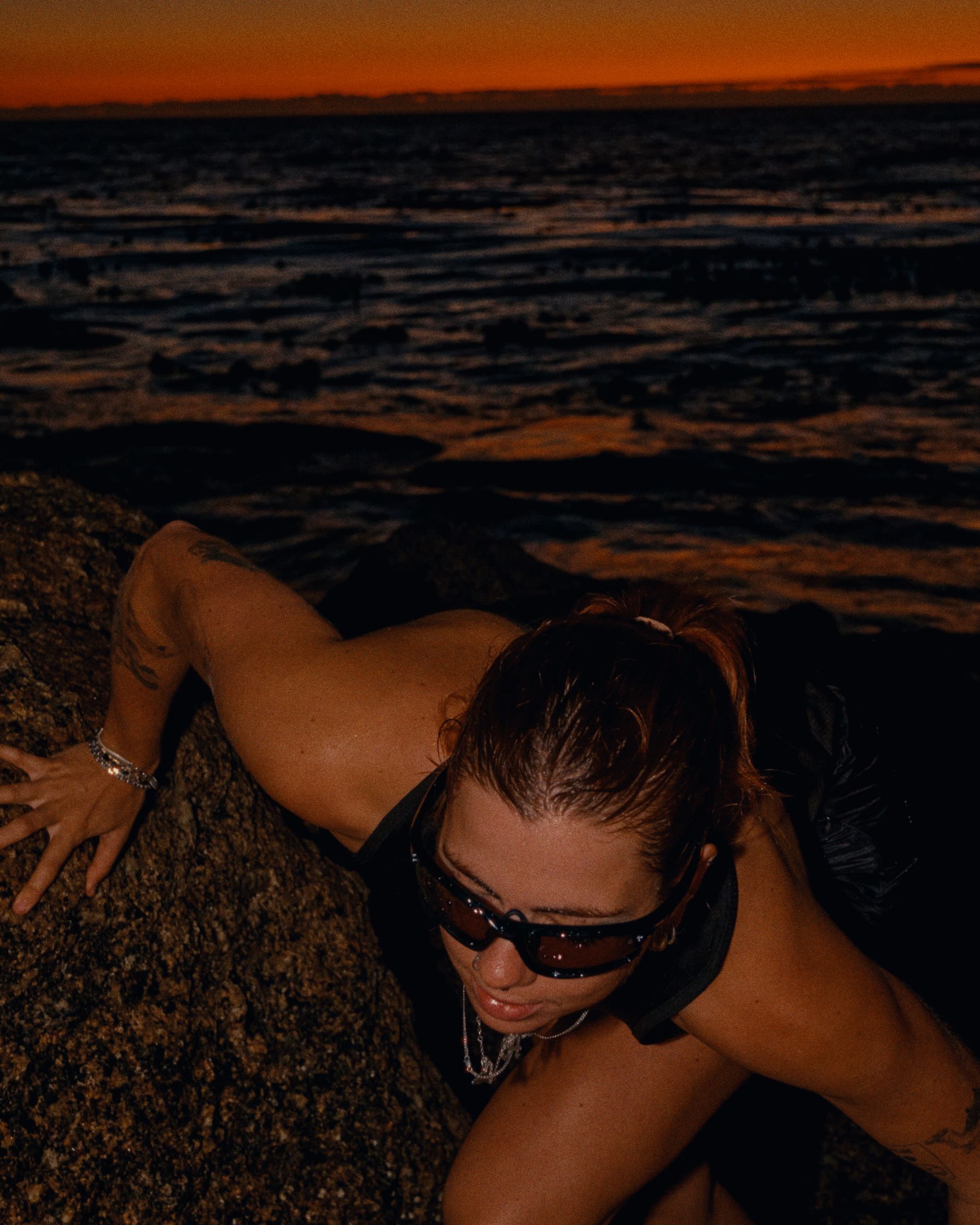 a woman crouching on a rock at sunset